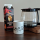 Carton of Fireball holiday nog, a coffee mug, and a pot of coffee on a wooden table